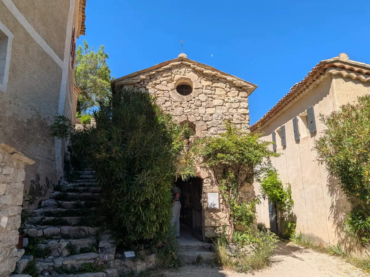 Facciata di pietra della cappella dei Penitenti bianchi, con oculo e vegetazione attorno alla porta