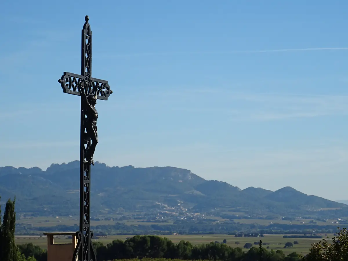 Ein eisernes Kreuz im Vordergrund und die Grate der Dentelles de Montmirail hinter den Weinbergen, von Cairanne aus gesehen