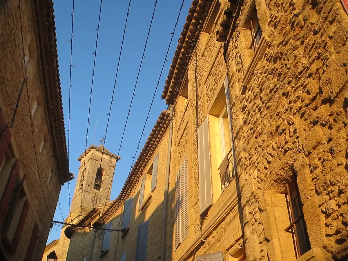 Steinfassaden und Kirchturm in einer Gasse von Châteauneuf-du-Pape im Abendlicht