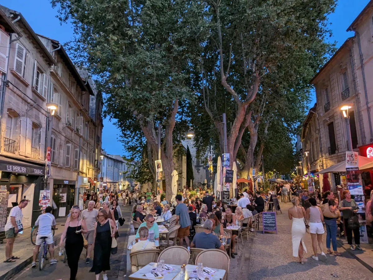 Terrasses et passants place des Corps-Saints au début d’une soirée de Festival à Avignon