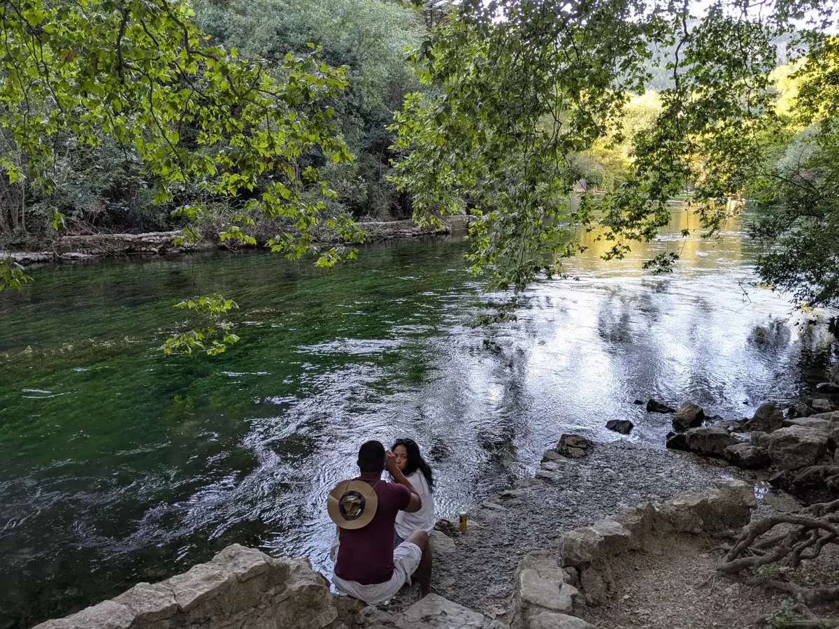 Besucher am Ufer der Sorgue in Fontaine-de-Vaucluse unter den Bäumen