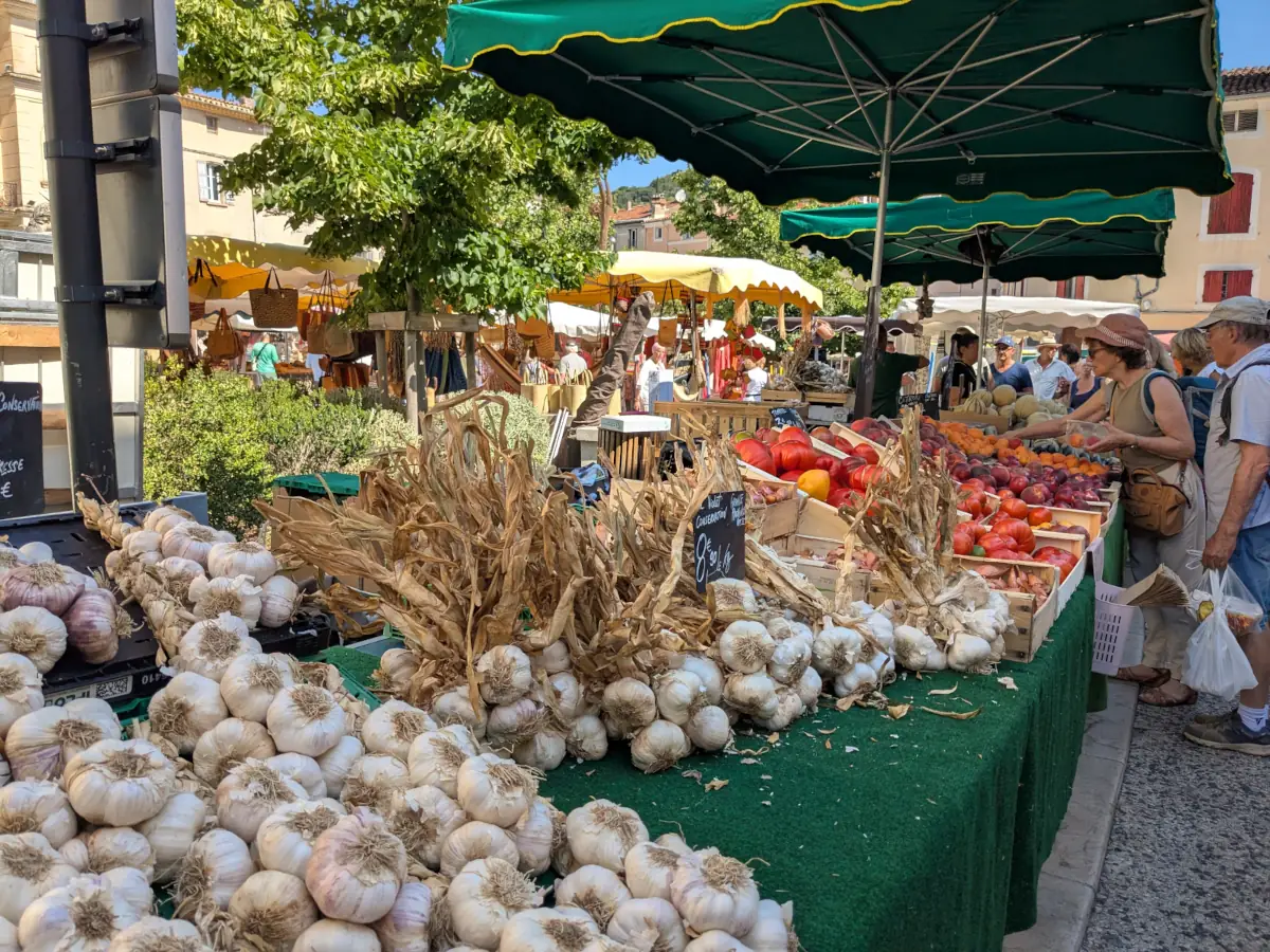 Garlic bulbs in the foreground of a fruit and vegetable stall at Apt’s market