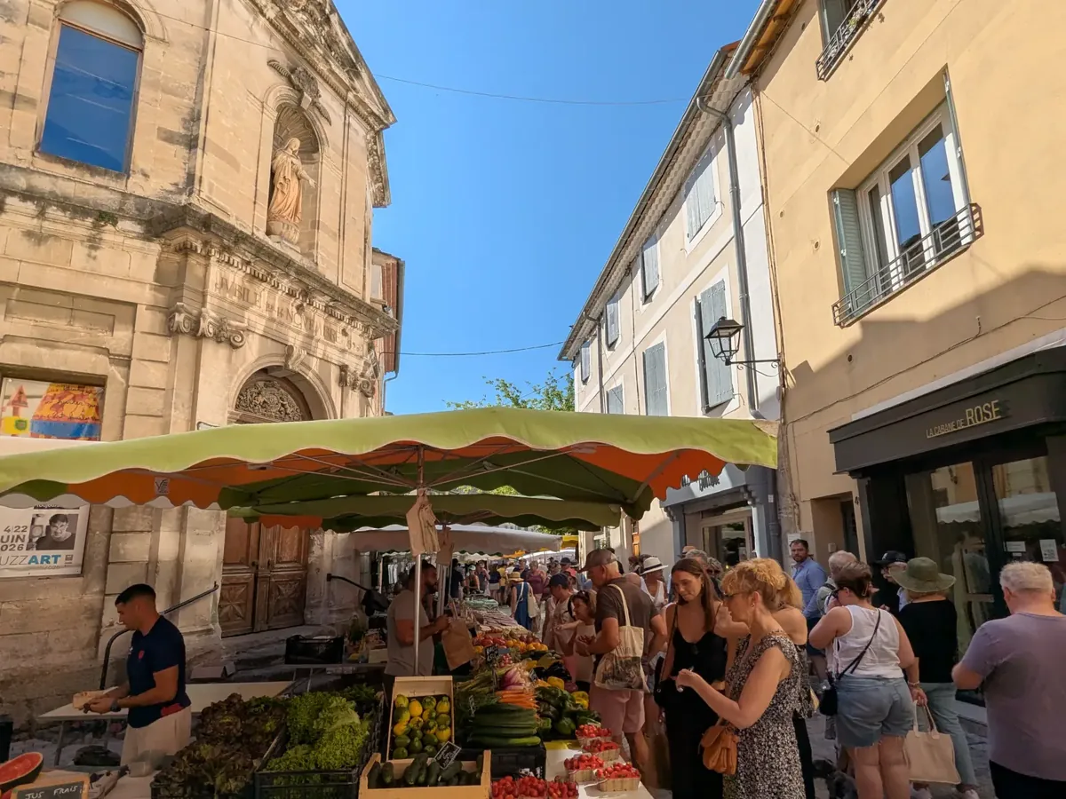 Portal der Stiftskirche Notre-Dame-des-Anges hinter den Marktständen in einer Straße von L’Isle-sur-la-Sorgue