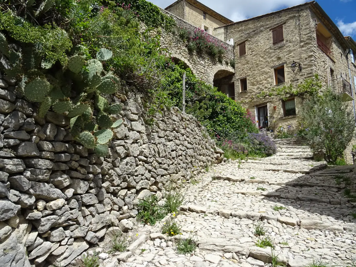 Calade en pente bordée de murs de pierre, de maisons et de plantes à Montbrun-les-Bains