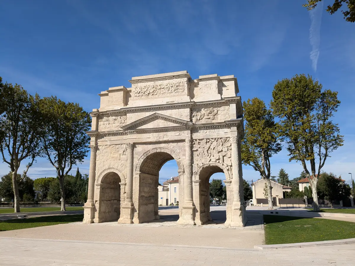 The Triumphal Arch of Orange, its three passageways and carved reliefs, in a tree-lined square