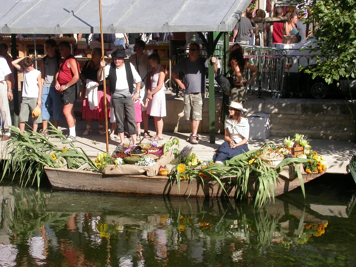 Mit Blumen geschmückter und beladener nègo-chin an einem Kai während des schwimmenden Markts von L’Isle-sur-la-Sorgue