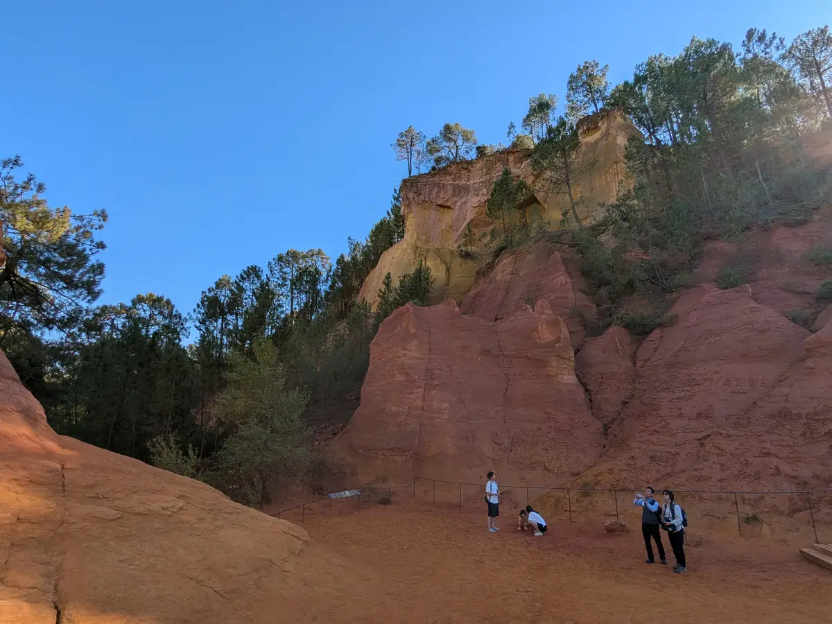 Visitors at the foot of a tall yellow and red cliff on the Sentier des Ocres