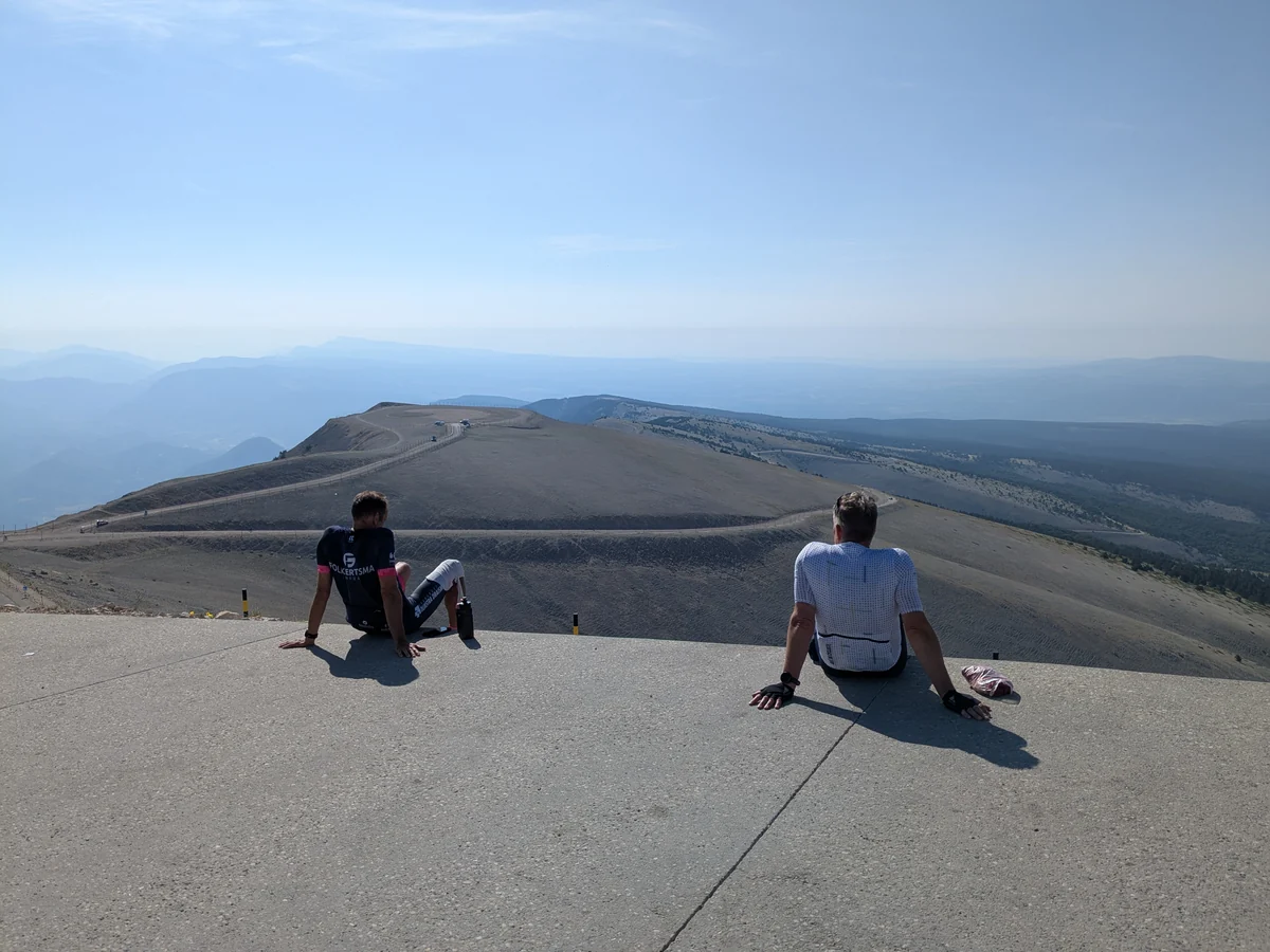 Deux cyclistes assis au sommet face aux lacets et aux reliefs lointains