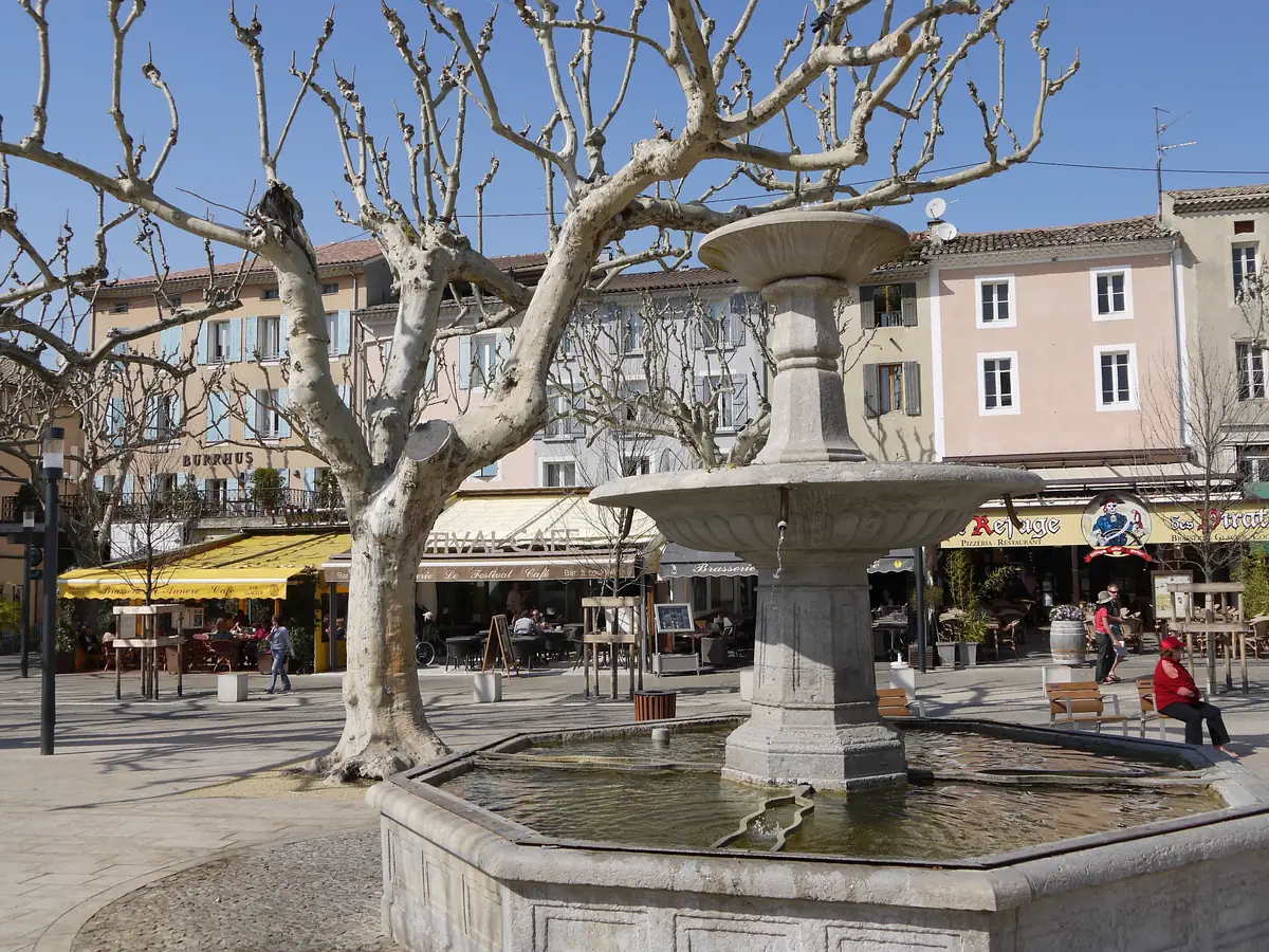 Brunnen auf der Place Montfort in Vaison-la-Romaine vor Caféterrassen und farbigen Fassaden