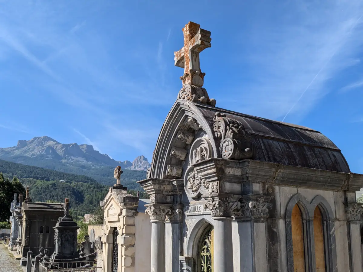 A funerary chapel with columns and a barrel roof in Barcelonnette cemetery, the crests of the Ubaye behind